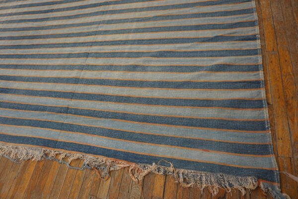 A flatweave rug featuring wide blue stripes and thin orange lines is displayed on rustic wood floors.