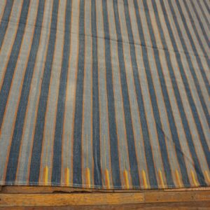 Vertical striped rug in dark blue, light blue, and orange lays over rustic wood flooring.