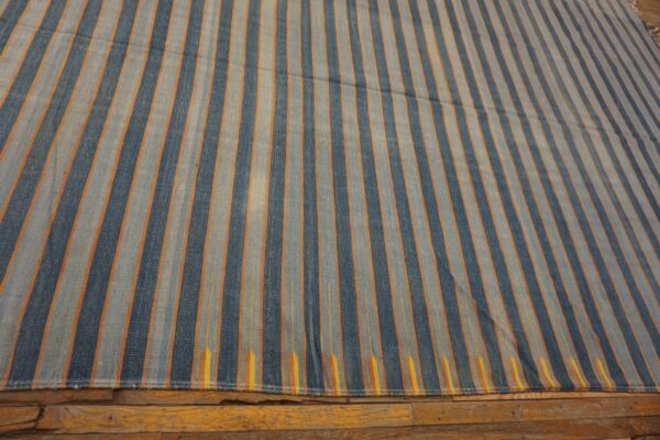 Vertical striped rug in dark blue, light blue, and orange lays over rustic wood flooring.