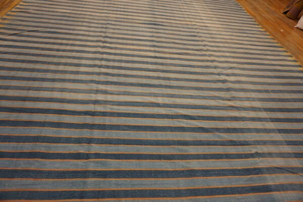 Striped blue and orange low-pile rug lying on a glossy light brown hardwood floor.