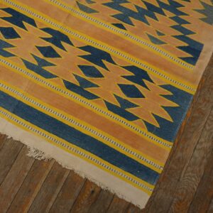 Blue, yellow, and orange flatweave rug with jagged geometric patterns lies on distressed wood floors.