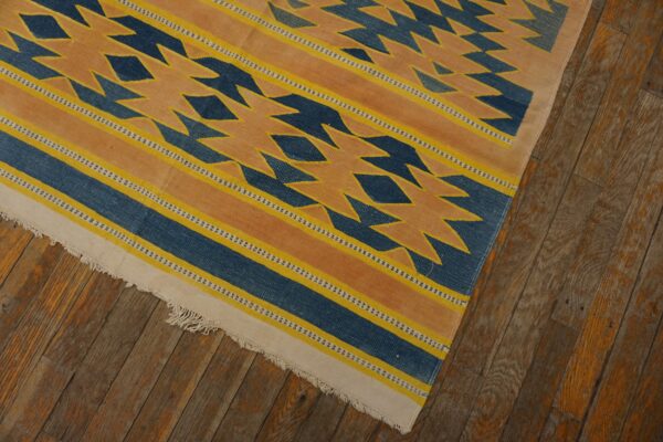 Blue, yellow, and orange flatweave rug with jagged geometric patterns lies on distressed wood floors.