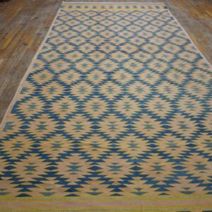 Blue and beige flatweave rug featuring a serrated diamond pattern displayed on worn wood planks.