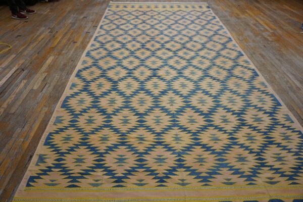 Blue and beige flatweave rug featuring a serrated diamond pattern displayed on worn wood planks.