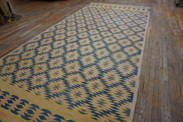 Long flatwoven rug featuring blue and yellow repeating geometric patterns on a cream ground over distressed wooden floors.