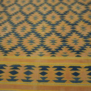 Geometric navy blue and gold flatweave rug displays alternating tribal patterns on a dark wood floor.