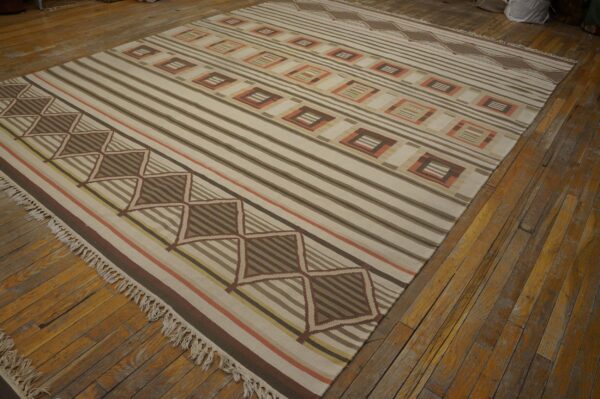 Large neutral flatweave rug featuring brown stripes and terra cotta geometric patterns on wood planks.