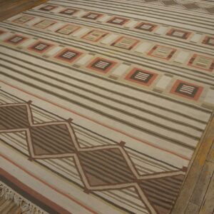 Tan flat-weave rug featuring brown stripes and geometric diamond and square patterns on a wood floor.