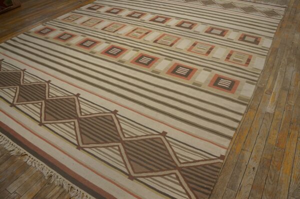 Tan flat-weave rug featuring brown stripes and geometric diamond and square patterns on a wood floor.