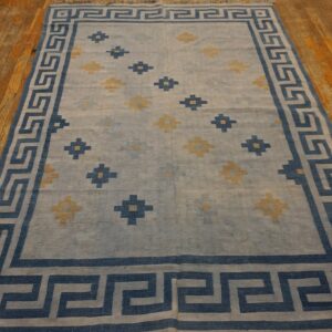 A blue and pale yellow rug with a Greek key border rests on rustic wood floors.