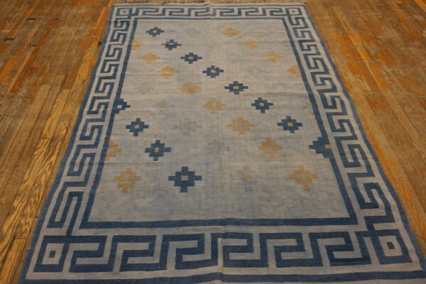 A blue and pale yellow rug with a greek key border rests on rustic wood floors.