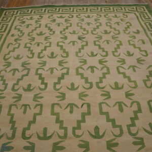 Large beige flatweave rug with green geometric patterns and a Greek key border on a rustic wood floor.
