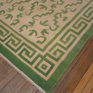 Green and beige rug with a Greek Key border and abstract field pattern rests on worn wood flooring.