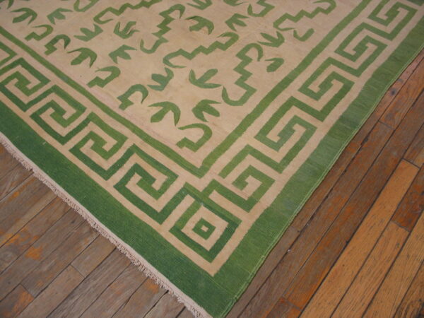 Green and beige rug with a greek key border and abstract field pattern rests on worn wood flooring.