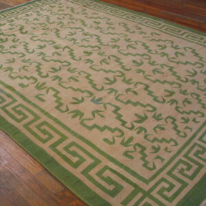 Low profile beige rug with green abstract patterns and a classic Greek key border on hardwood floors.