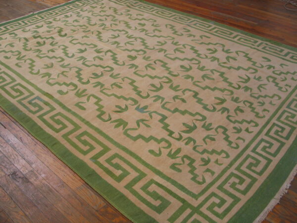 Low profile beige rug with green abstract patterns and a classic greek key border on hardwood floors.