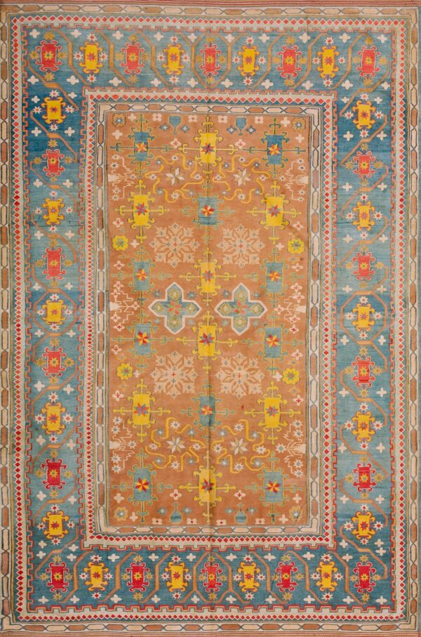 Rust and blue geometric rug with yellow and red patterns displayed on distressed wooden flooring.