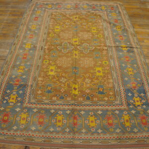 Geometric camel and dusty blue rug with yellow and red patterns displayed on a weathered wood floor.