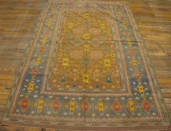 Geometric camel and dusty blue rug with yellow and red patterns displayed on a weathered wood floor.