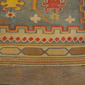 Multi-colored flatweave rug featuring geometric red, blue, and cream borders atop rustic wood planks.