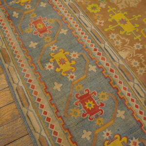 Flatweave rug section featuring blue, rust, red, and yellow stylized geometric designs on distressed wood flooring.