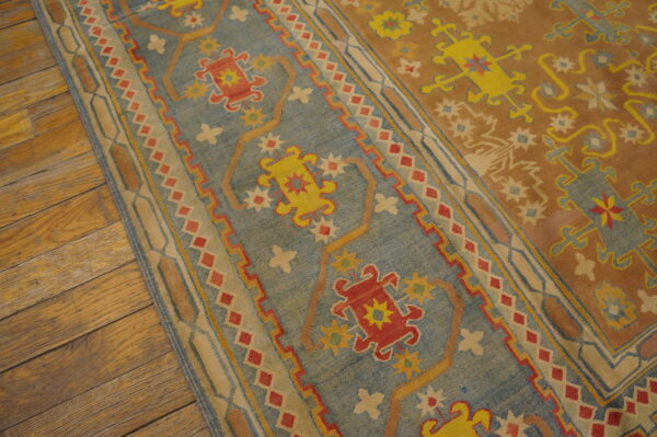 Flatweave rug section featuring blue, rust, red, and yellow stylized geometric designs on distressed wood flooring.