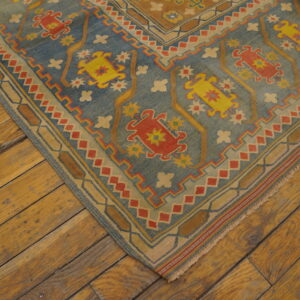 A corner of a blue, red, and yellow geometric rug rests on distressed amber-toned wood plank flooring.