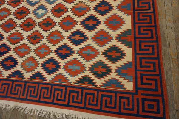 Low-pile rug in rust, navy, and cream, featuring stepped geometric designs and a bold greek key border.