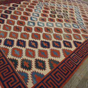 Geometric rug in cream, rust, and blue with a Greek key border resting on weathered wood floorboards.