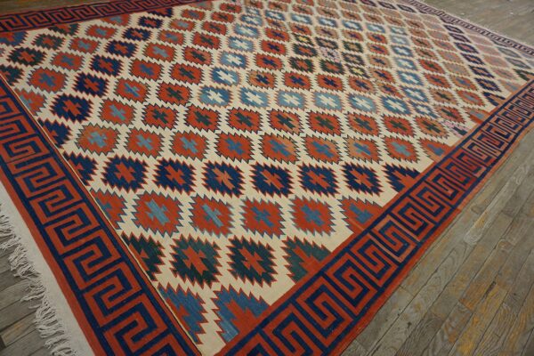 Geometric rug in cream, rust, and blue with a greek key border resting on weathered wood floorboards.