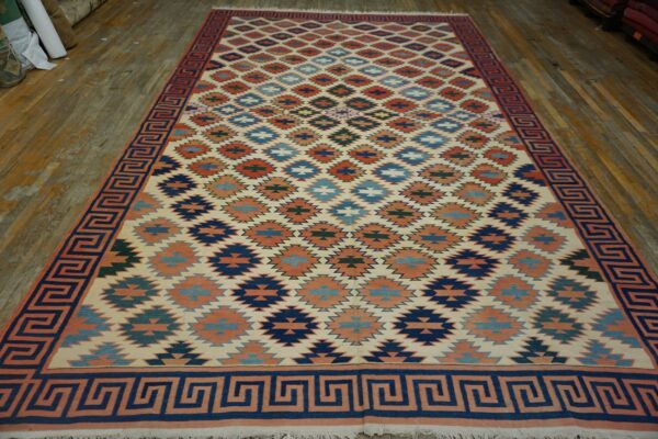 Flatweave rug with multicolor geometric patterns and a navy greek key border on wood flooring.