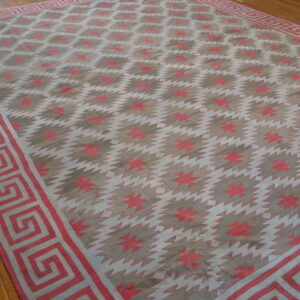 A large, low-pile rug featuring red, gray, and white sawtooth patterns and a Greek key border on wood flooring.