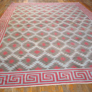 Large flatweave rug with jagged geometric patterns and a red meander border on polished hardwood flooring.