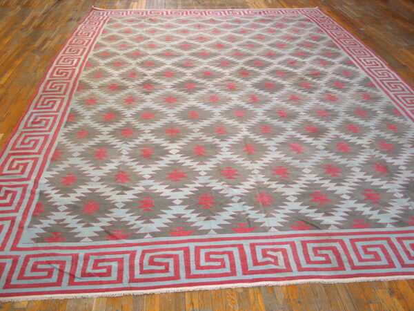 Large flatweave rug with jagged geometric patterns and a red meander border on polished hardwood flooring.