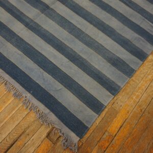 Diagonal dark and light blue striped low-pile rug with fringe lies on distressed orange plank wood floors.