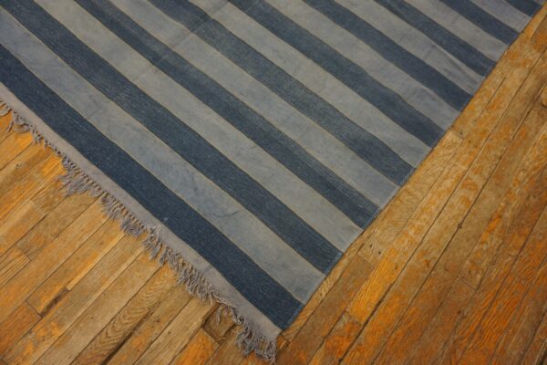 Diagonal dark and light blue striped low-pile rug with fringe lies on distressed orange plank wood floors.