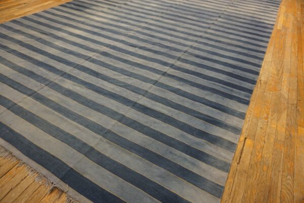 Large rug with alternating navy and slate blue horizontal stripes on distressed wood planks.