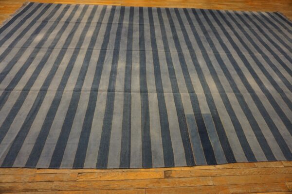 A low-pile rug with alternating dark blue and light blue vertical stripes covers rustic wood plank flooring.