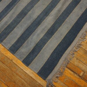 Diagonal blue and gray striped rug with fringe covers part of an aged, orange-toned wooden floor.