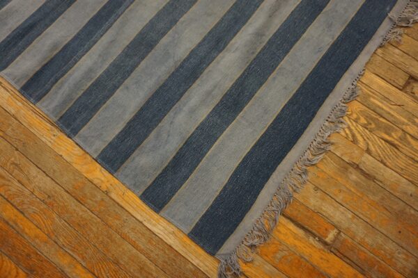 Diagonal blue and gray striped rug with fringe covers part of an aged, orange-toned wooden floor.