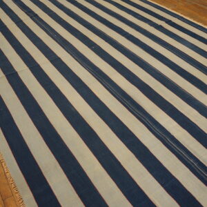 Wide navy and cream striped rug with thin red accents lies on a textured wood floor.
