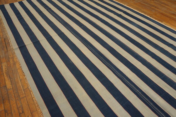 Wide navy and cream striped rug with thin red accents lies on a textured wood floor.