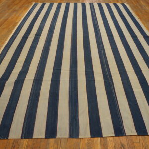 Flatweave rug with bold vertical navy blue and beige stripes lying on glossy hardwood planks.