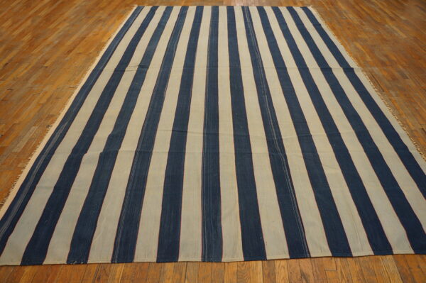 Flatweave rug with bold vertical navy blue and beige stripes lying on glossy hardwood planks.