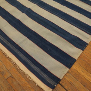 A flatwoven rug with wide cream and indigo stripes and fringe rests on rustic wood plank flooring.