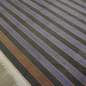 Striped flatweave rug featuring blue and dark grey bands accented by thin rust lines on weathered wood flooring.