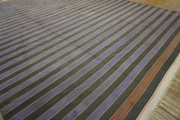 Low-pile rug with alternating dark gray and muted blue diagonal stripes resting on wood flooring.