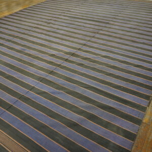 Wide blue and black striped flatweave rug with thin separating lines rests on a rustic wood floor.