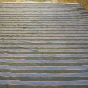 A large rug with horizontal blue and dark green stripes separated by thin orange lines rests on a wood floor.