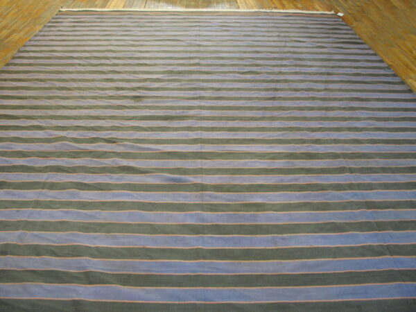 A large rug with horizontal blue and dark green stripes separated by thin orange lines rests on a wood floor.